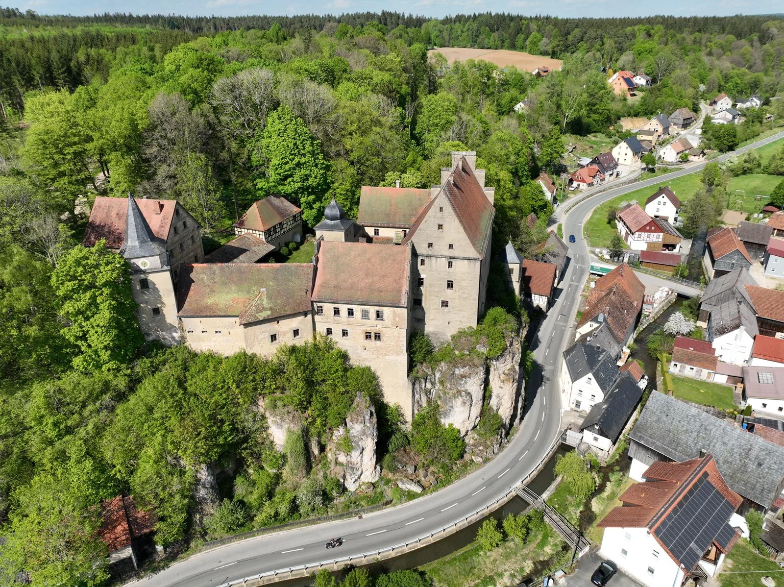 Schloss Wiesentfels auf seinem Felsen, umgeben von Wald und dem Dorf im Wiesenttal